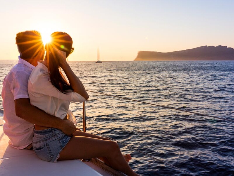 Couple sitting on catamaran sailing in to the sunset in the caldera Santorini